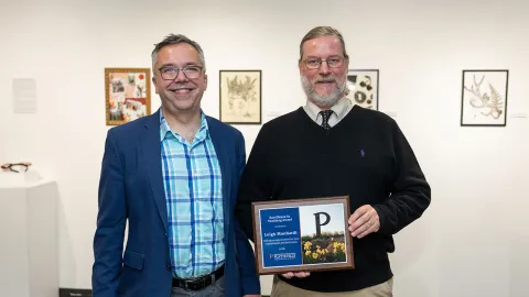 Two men standing against a while background, one is holding an award.