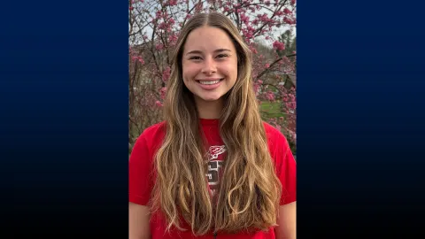 Smiling woman in red shirt standing in front of cherry blossom tree
