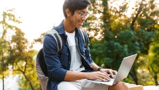 student sitting outside working on laptop